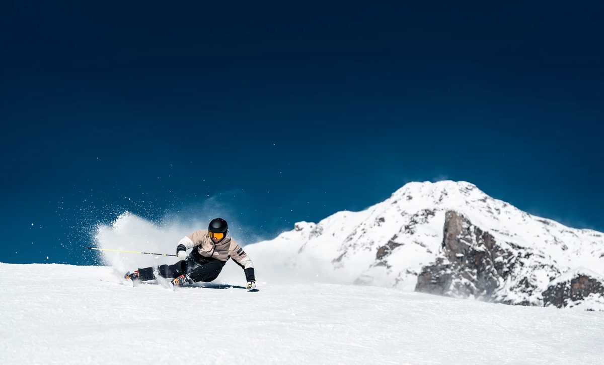 Skier carving a turn on a snowy slope with a rocky alpine peak behind